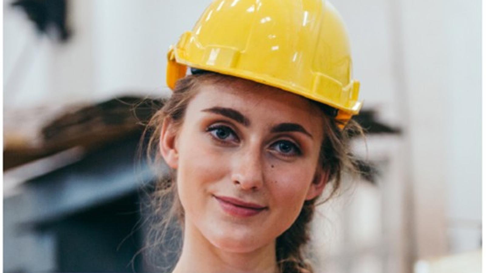 girl wearing a hard hat holds her laptop 