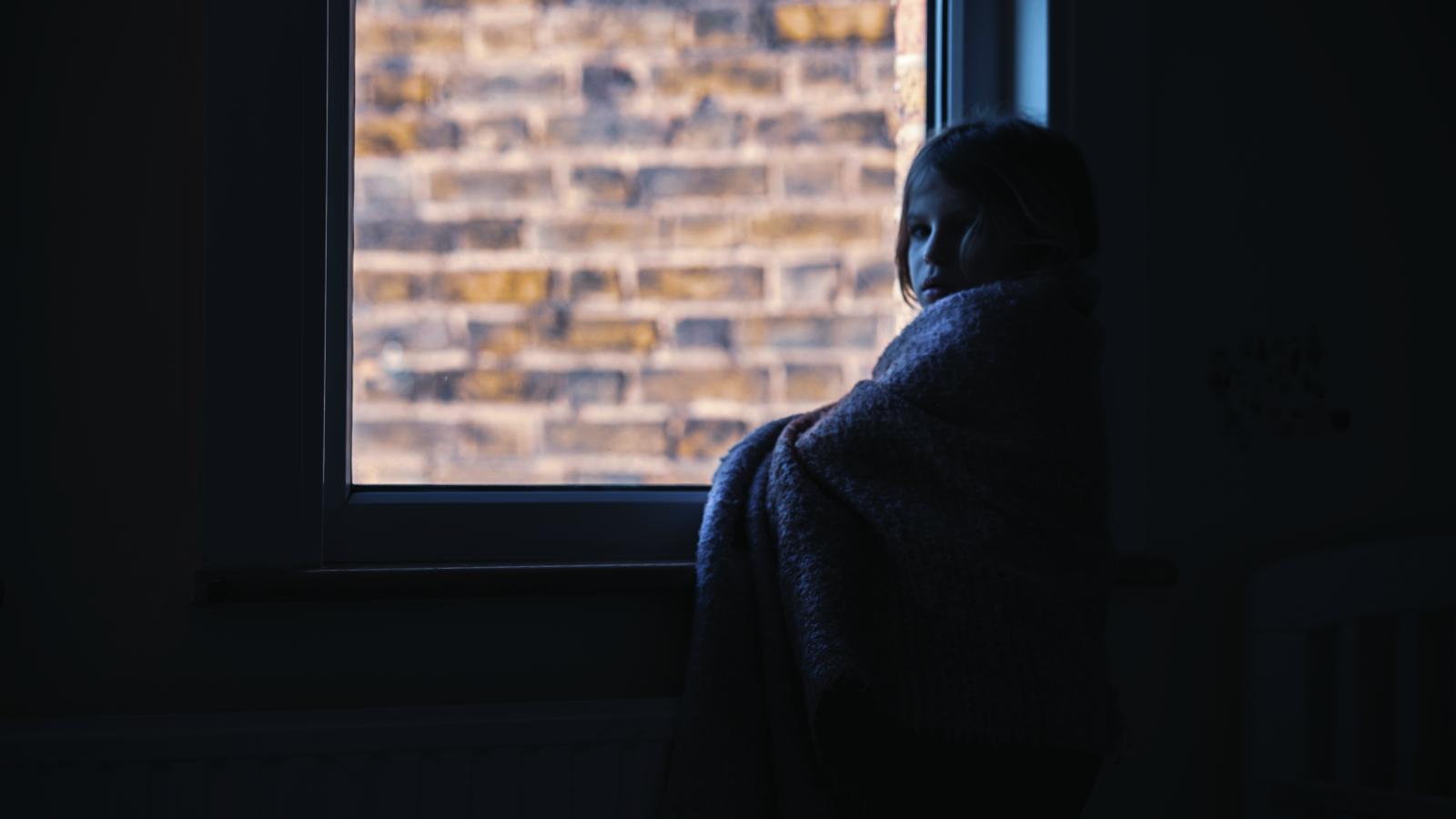 A girl wrapped in a blanket looking out a window