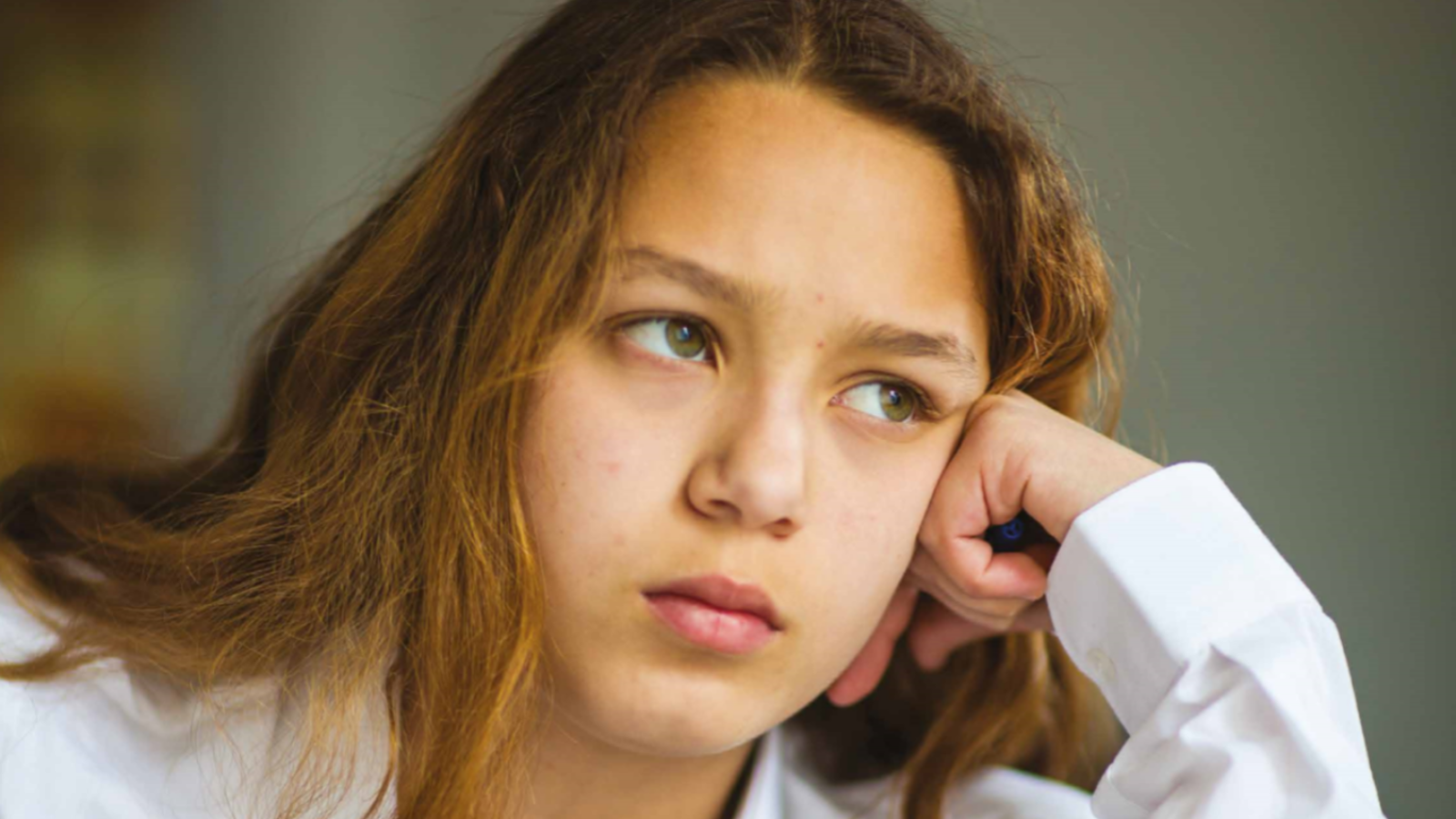 Girl in school uniform resting head on her hand while looking into the distance