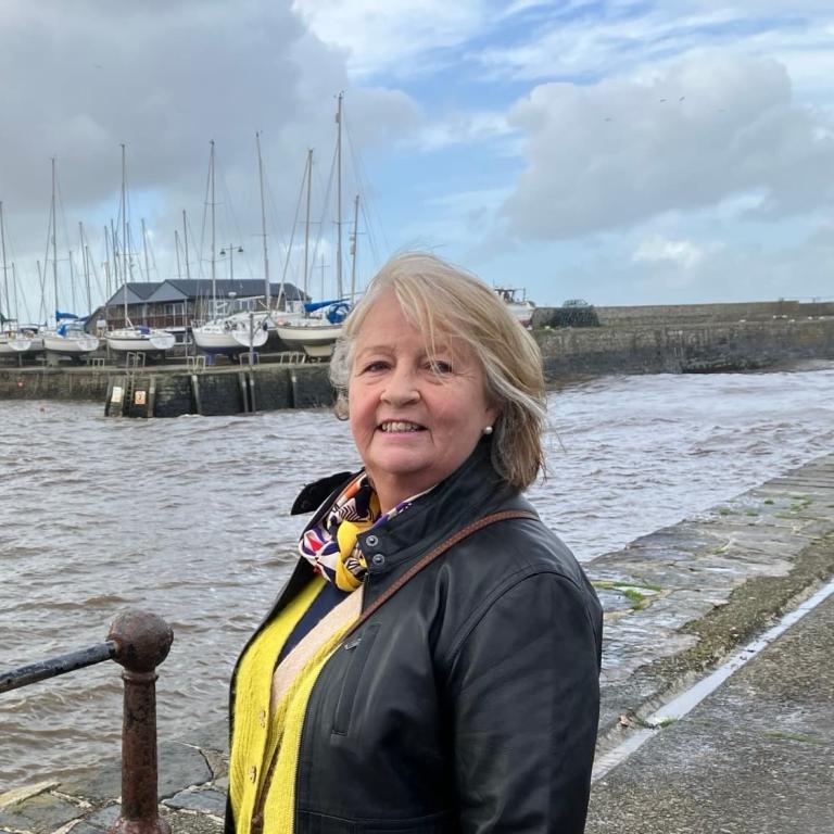 Foster carer Bridget stands smiling with a harbour in the background