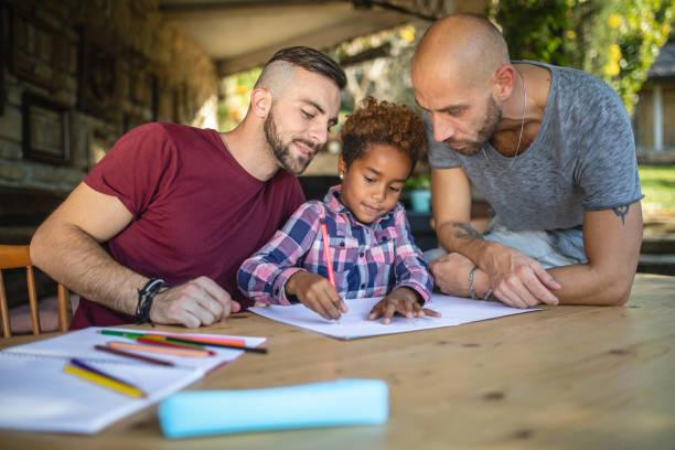 Two dads and a young child, at a table colouring together