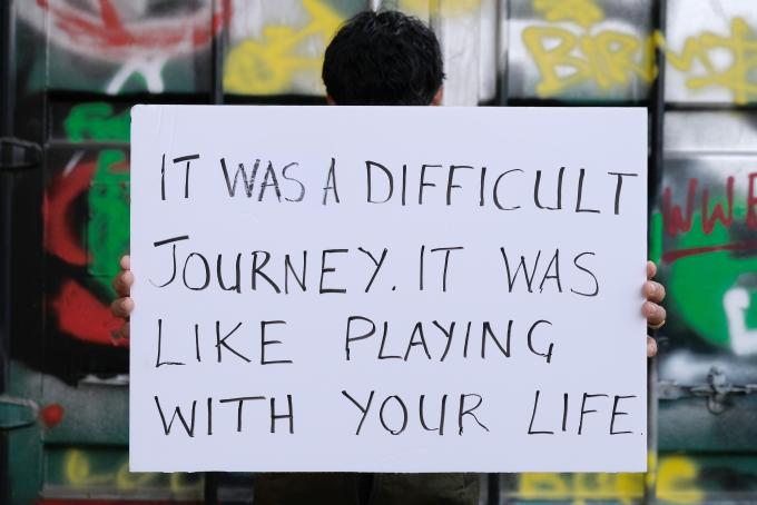 Boy holds a sign that says "It was a difficult journey. It was like playing with your life"