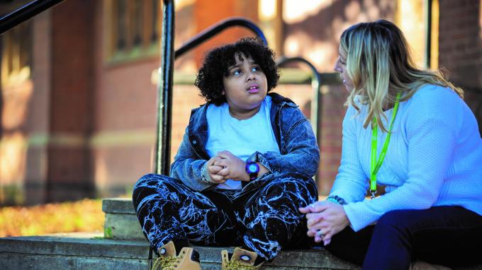 A young person sits on a step in conversation with a Barnardo's support worker